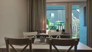 Un comedor con una mesa y sillas, una ventana con cortinas y vistas a una casa y jardín.
