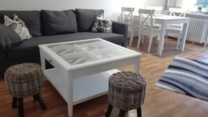 Una sala de estar moderna con un sofá gris, una mesa de centro blanca, taburetes de mimbre y un tapete a rayas.
