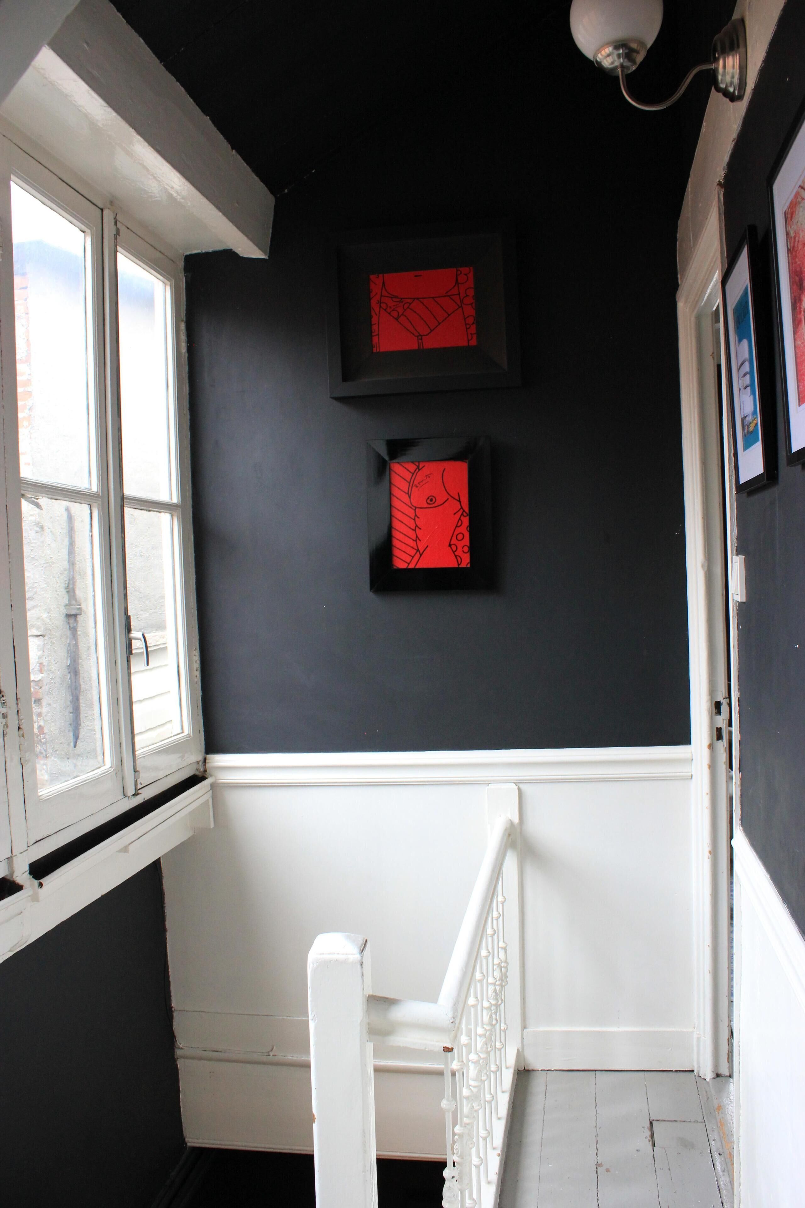 Een trap met witte leuningen die leidt naar een donkere kamer met twee kunstwerken met rode lijsten aan de muur.
