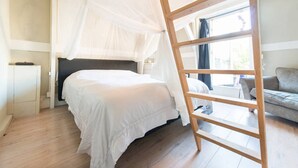 Une chambre à coucher avec un lit à baldaquin, une échelle en bois, un canapé et une fenêtre avec des rideaux.