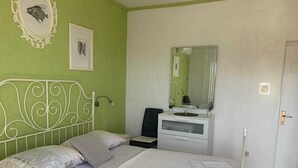 Een slaapkamer met een bed, nachtkastje, stoel, kapstok en spiegel.