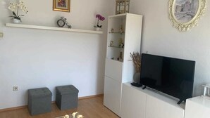 Een woonkamer met een flatscreen televisie, witte planken met decoratieve items, en een lijst met een schilderij aan de muur.