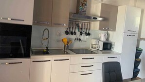 Een moderne keuken met witte kasten, een zwart fornuis, een spoelbak met kraan en een magnetron.