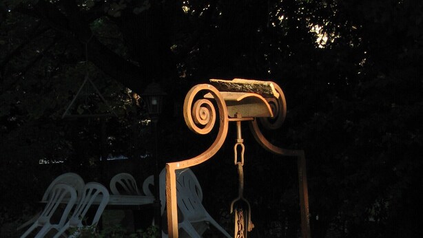 Un jardín con una escultura de metal, plantas en macetas y asientos de piedra.