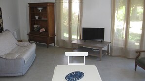 Una sala de estar con sofá, televisor sobre un mueble bajo, aparador de madera y ventana con cortinas.