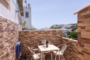 Ein Balkon mit Tisch und Stühlen, einer Weinflasche und einem Gartenschlauch.