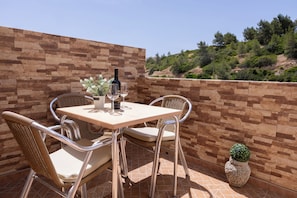 Un patio exterior con un muro de piedra, una mesa con sillas, una botella de vino y una planta en maceta.
