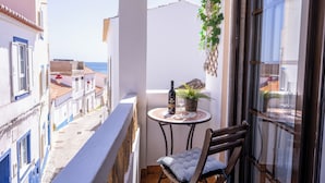A balcony with a table, chair, potted plant, and a bottle of wine.