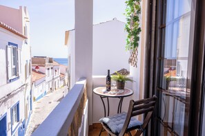 A balcony with a table, chair, potted plant, and a bottle of wine.