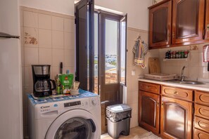 Una cocina compacta con lavadora, cafetera y un pequeño cubo de basura.