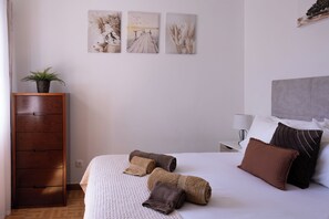 Ett hotellrum med en säng, kuddar, ett nattduksbord, en lampa och konst på väggen.