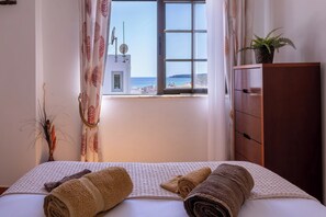 Un dormitorio con cama, cómoda, ventana con vista al mar y una planta sobre la cómoda.