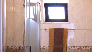 A bathroom with a glass shower enclosure, a toilet, and a towel rack with towels.
