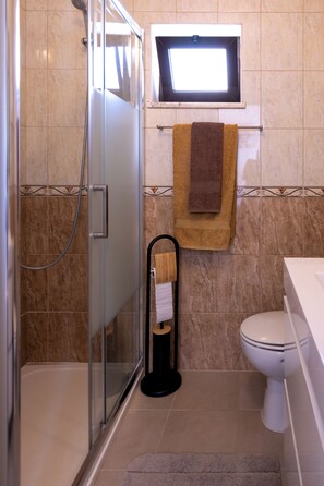 A bathroom with a glass shower enclosure, a toilet, and a towel rack with towels.