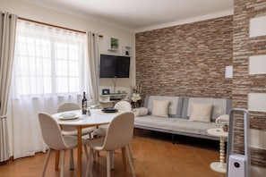 Ein modernes Wohnzimmer mit Steinwand, Flachbildfernseher, einer Couch und einer Essecke mit Stühlen und Tisch.