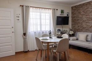 Un comedor con una mesa lista para dos personas, un sofá, un televisor de pantalla plana y un muro decorativo.
