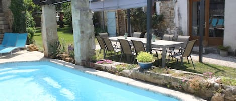 Un área de piscina con una pérgola, mobiliario exterior y una pared de piedra.