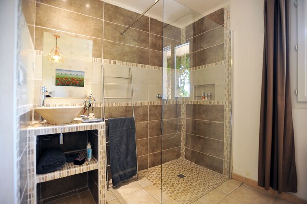 A bathroom with a glass-enclosed shower, a large mirror, and a sink with a bowl basin.