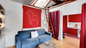 A loft-style living space with a blue sofa, a red accent wall, and a skylight. - BRAGORA SMOOCHY ATTIC VENICE M0270423479 (Venice)