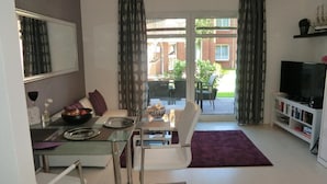 Ein modernes Wohnzimmer mit einem Glastisch, einem weißen Sofa und einem Fernseher auf einem Standfuß.