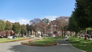 Ein Innenhof mit einem zentralen Rasen, Bänken und einem Gebäude mit Rundbogenfenstern im Hintergrund.