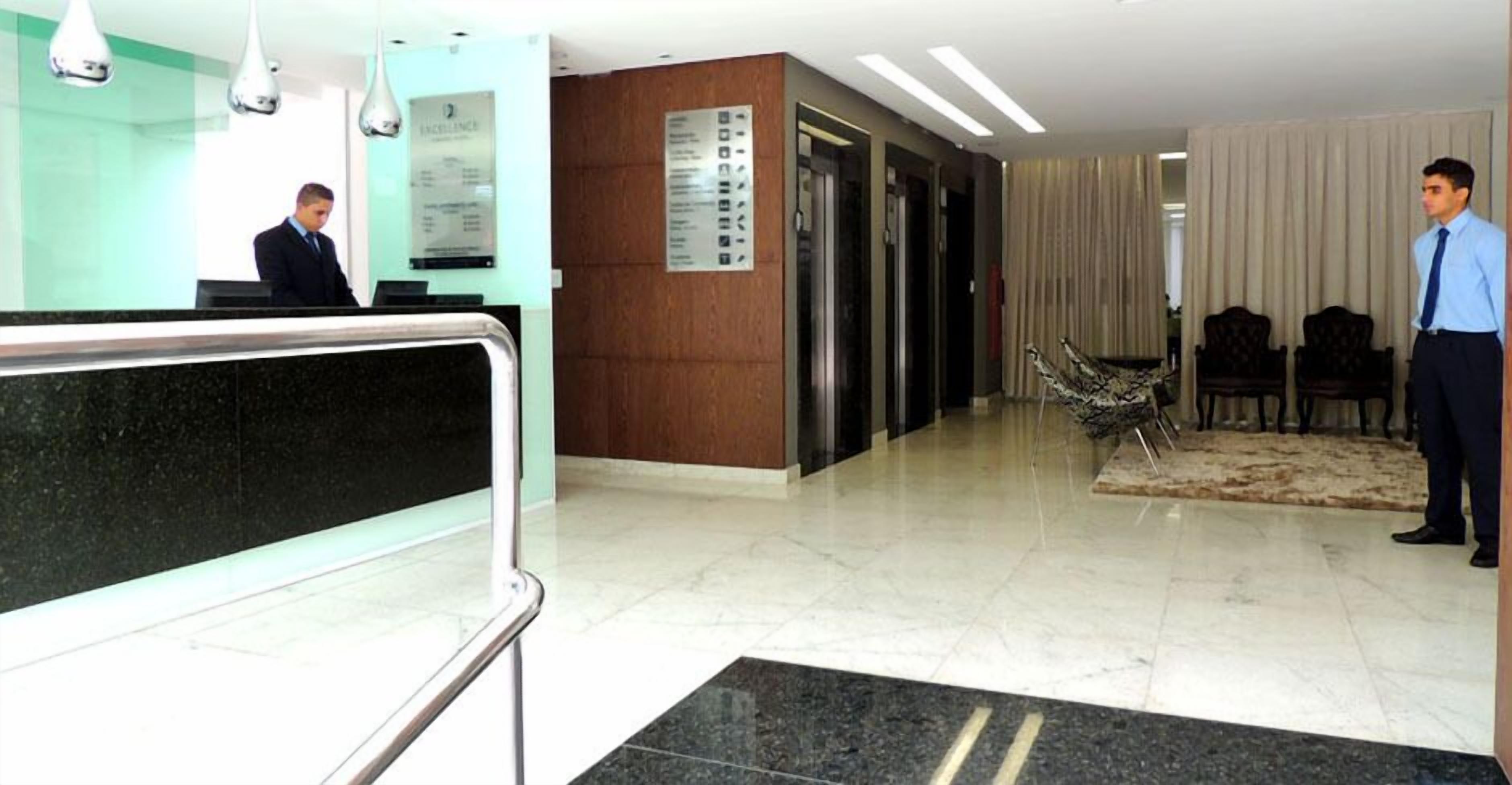 Un vestíbulo de hotel con mostrador de recepción, una zona de espera con sillas y un mostrador de atención al cliente.