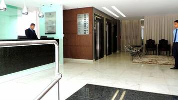 Un vestíbulo de hotel con mostrador de recepción, una zona de espera con sillas y un mostrador de atención al cliente.