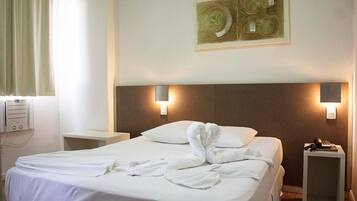 Una habitación de hotel con una cama bien hecha, dos mesitas de noche, una obra de arte en la pared y un ventanal con cortinas.
