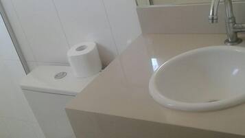 Casa de banho com lavatório branco, sanita e um contentor de lixo.