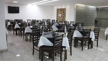 Un comedor con varias mesas y sillas, un televisor de pantalla plana montado en la pared y un cuadro abstracto grande.