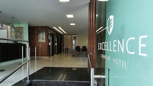 En hotellobby med en trappa som leder upp till nästa våning, en receptionsdisk och en skylt med texten ”EXCELLENCE COMFORT HOTEL”.