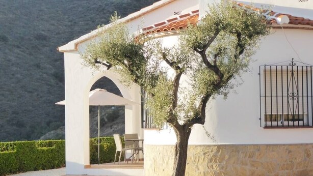 A white building with a stone base, a tiled roof, and a tree in front. - House with Private Pool (Herrera) (Arenas)
