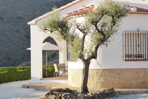 Un edificio blanco con base de piedra, techo de tejas y un árbol en frente.