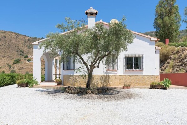 Un edificio blanco con techo de tejas, una chimenea y un árbol en primer plano.