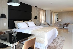 Una habitación de hotel moderna con una cama grande, una mesa de comedor y una zona de estar separada.