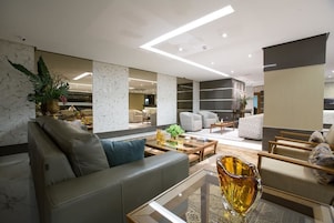 Una sala de estar moderna con sofá, sillones y una mesa de centro. Hay plantas y objetos decorativos sobre la mesa.