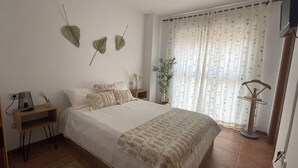 Et soveværelse med seng, sengeborde, lampe, en plante og et vindue med gardiner.