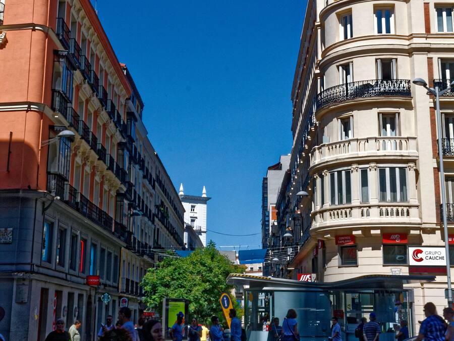 A busy urban street with historic buildings, a bus stop, and pedestrians.