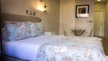 A neatly made bed with floral bedding, a small table, and a framed artwork on the wall.