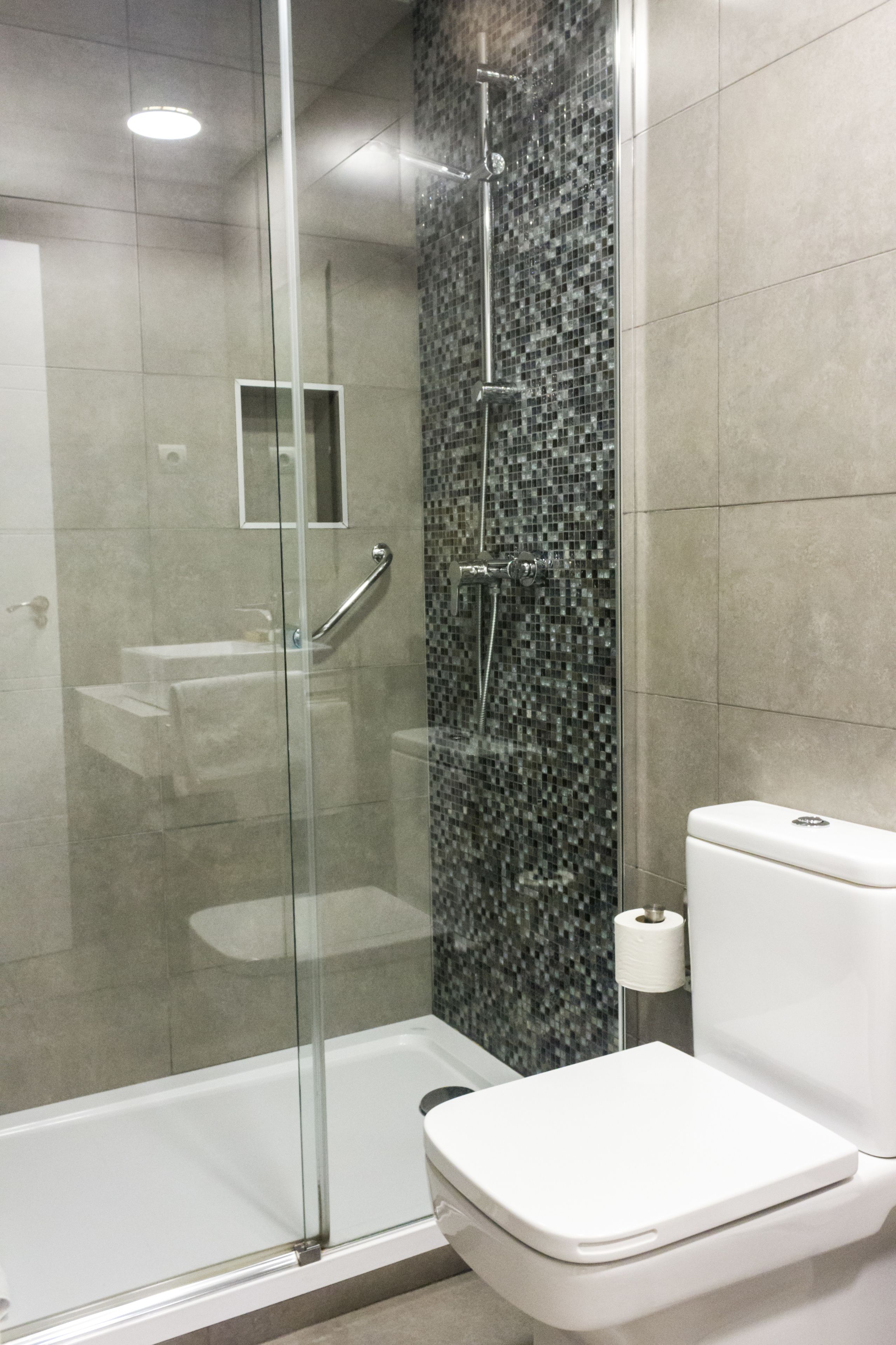 Un baño moderno con ducha envuelta en vidrio, inodoro blanco y salpicadero de azulejos.