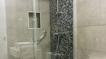 Un baño moderno con ducha envuelta en vidrio, inodoro blanco y salpicadero de azulejos.