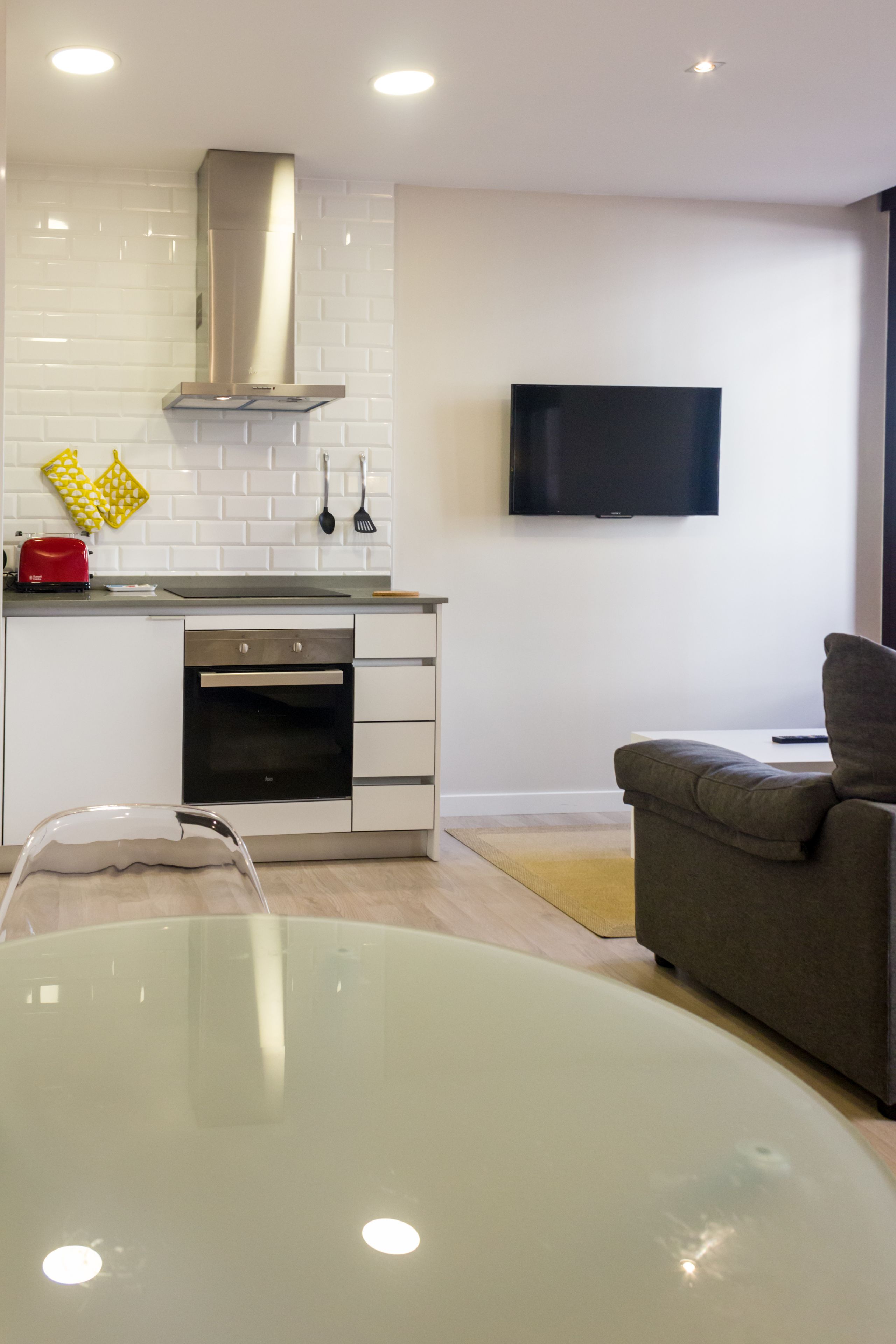 A modern kitchen with white cabinets, a stainless steel range hood, and a flat-screen TV mounted on the wall.
