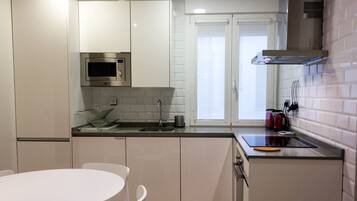 Una cocina moderna con armarios blancos, un microondas de acero inoxidable y una ventana sobre el fregadero.