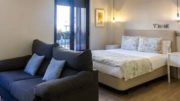 A modern bedroom with a sofa, a bed with floral bedding, a bedside table, and a wall-mounted light fixture.