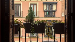 Un balcón con macetas, vistas de edificios cercanos y un cartel que indica disponibilidad.