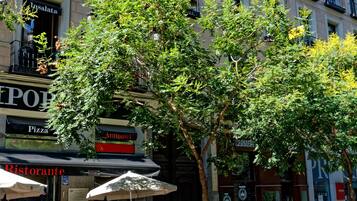 Un edificio con varios balcones, una tienda con letrero de pizza y un árbol al frente.