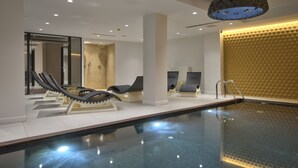 Un área de piscina interior moderna con sillones de descanso y una lámpara decorativa en el techo.
