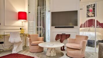 Una sala de estar moderna con un televisor, dos sillones rosa, una mesa redonda de mármol y una alfombra roja.