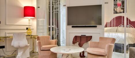 A modern living room with a TV, two pink armchairs, a round marble table, and a red rug.