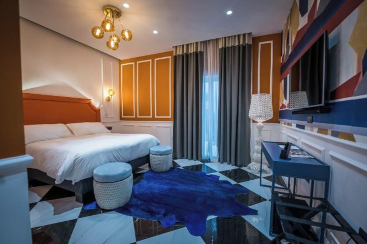 A hotel room with a bed, a desk, a chair, a rug, and a large mirror.